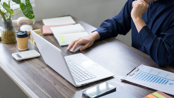 Photographer reviewing work on laptop at desk with smartphone, notes, and coffee