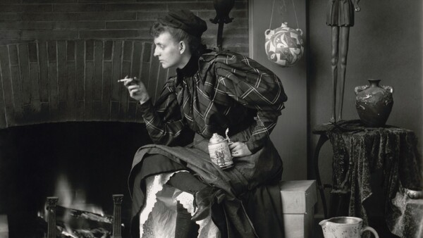 Woman in dark clothing sits by fireplace in vintage interior setting