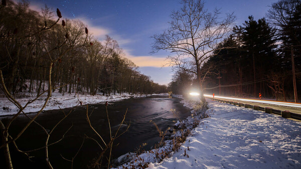 Winter landscape with unfrozen river flowing through snow-covered banks at twilight