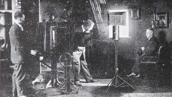 Studio film production setup with actors, lighting equipment, and crew members in vintage black and white photograph