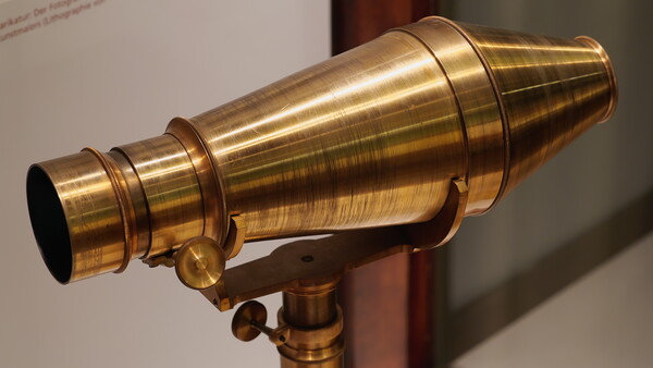 Vintage brass telescope with conical barrel and focusing mechanism mounted on tripod base