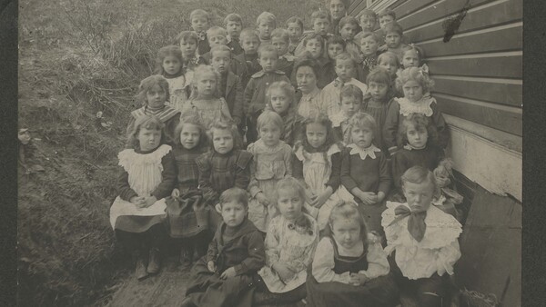 Large group portrait of approximately 40 children arranged in rows outside a building