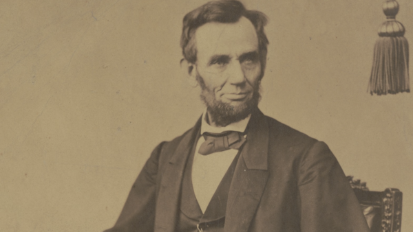 Sepia-toned vintage portrait of a bearded man in a dark suit and bow tie, seated and gazing toward the camera.