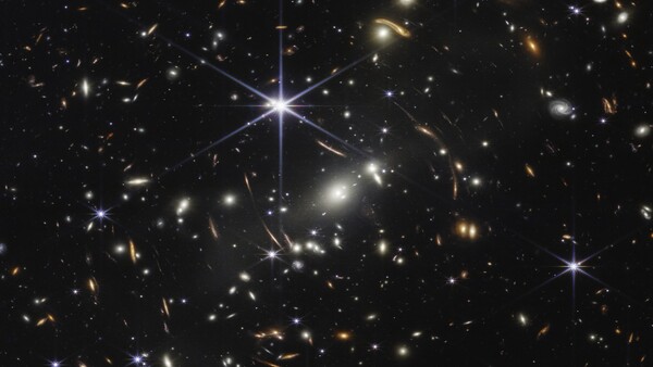 Deep space photograph showing distant galaxies and stars with gravitational lensing effects