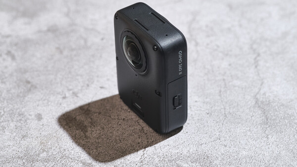 Black compact action camera with lens and side control button on concrete surface