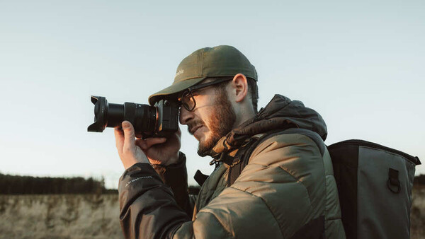 Photographer in tactical gear holding a telephoto lens camera to his face
