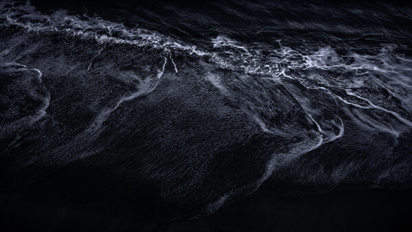 Aerial view of dark ocean water with white wave patterns and foam trails