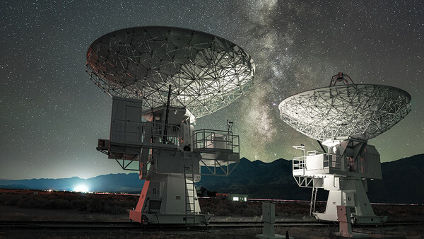 Two large radio telescope dishes under the Milky Way at night with moonrise on the horizon