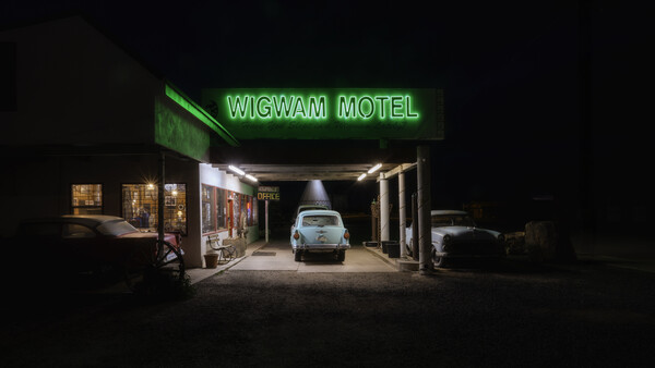 Wigwam Motel storefront at night with neon green sign and parked vintage car