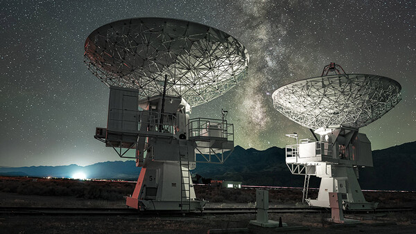 Two large radio telescope dishes pointing skyward beneath the Milky Way at night