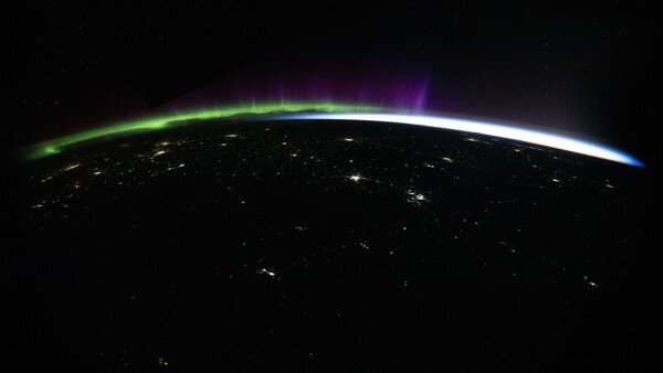Earth's horizon at night with aurora borealis and city lights from space