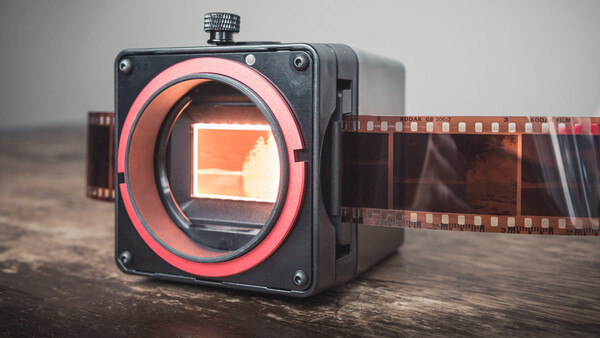 Medium format camera with red mirror assembly and film visible on wooden surface