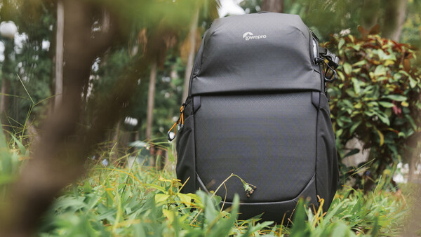 Black Lowepro camera backpack with orange zipper pulls resting on grass in a tropical garden.