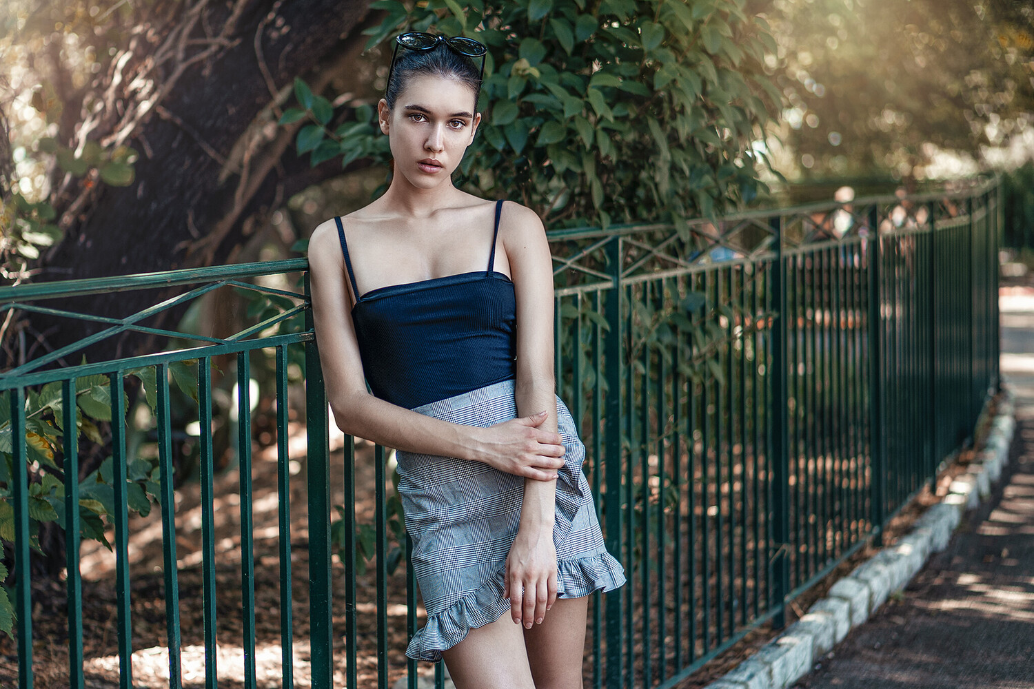 Woman in navy crop top and denim skirt posing against green fence with ivy