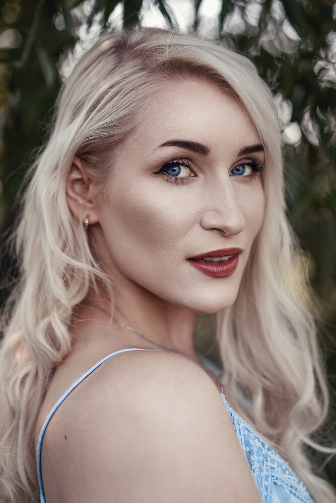 Portrait of a woman with platinum blonde wavy hair and red lipstick, looking over her shoulder