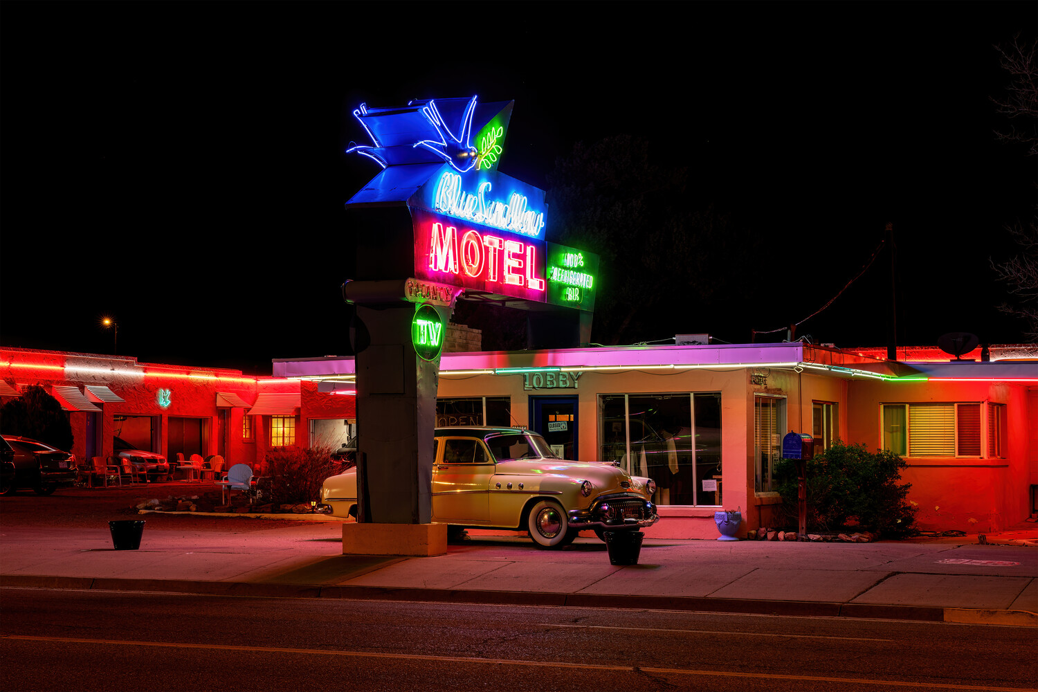 Vintage motel at night with neon blue and red signage, classic car parked in front