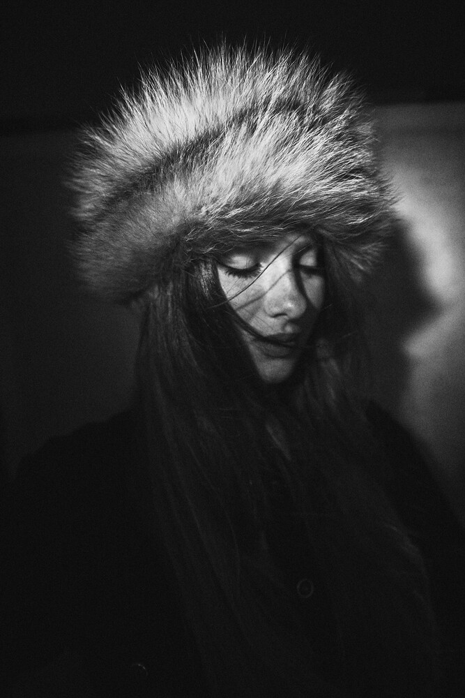 Person wearing oversized fur hat and sunglasses in dramatic black and white portrait