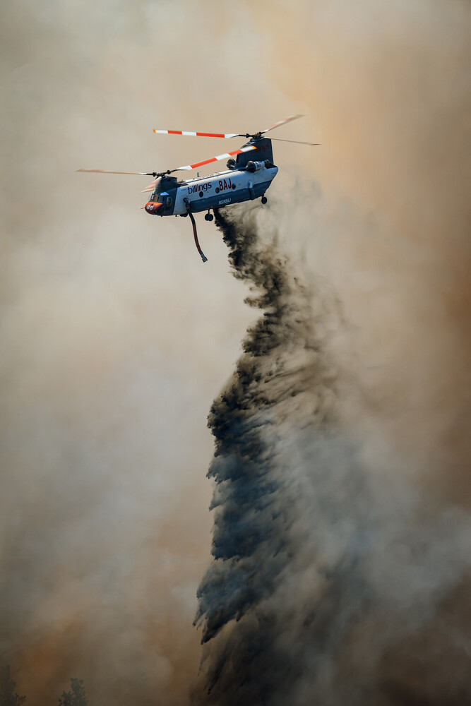 Blue helicopter releasing water or fire retardant in dense smoke