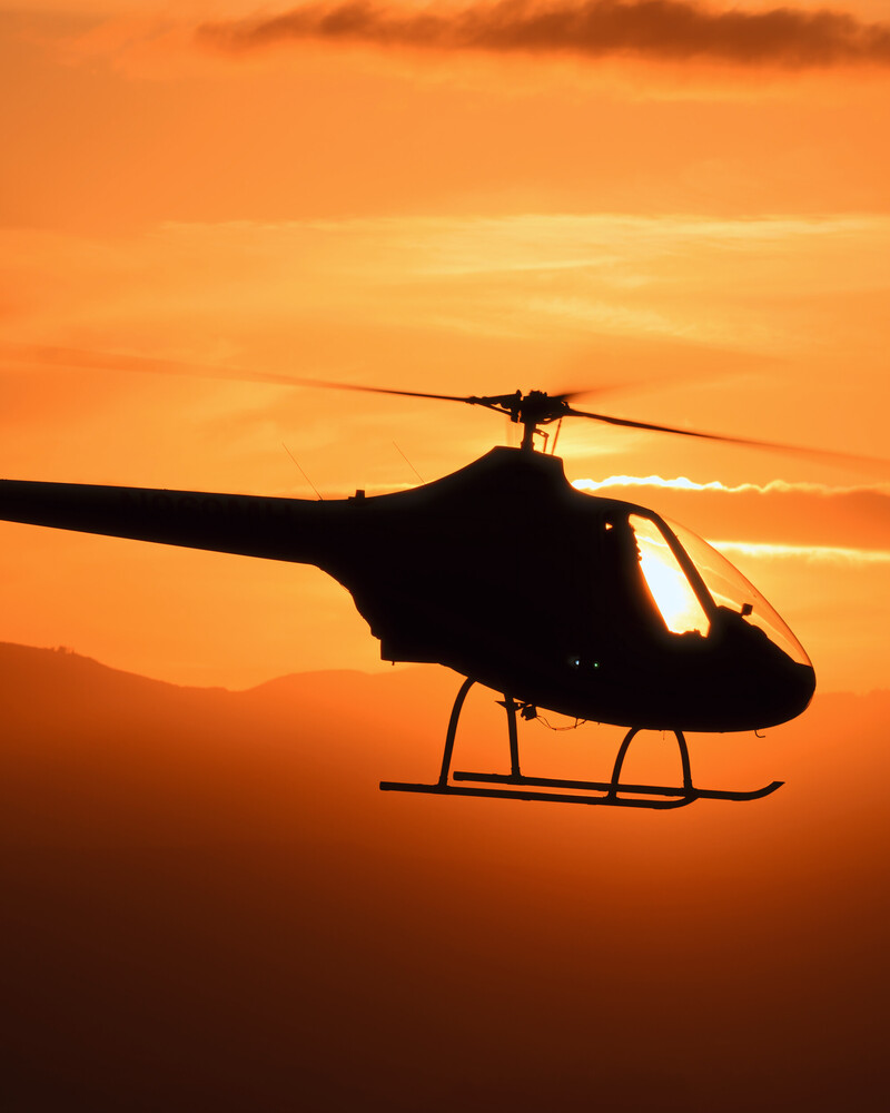 Helicopter silhouetted against orange sunset sky during golden hour