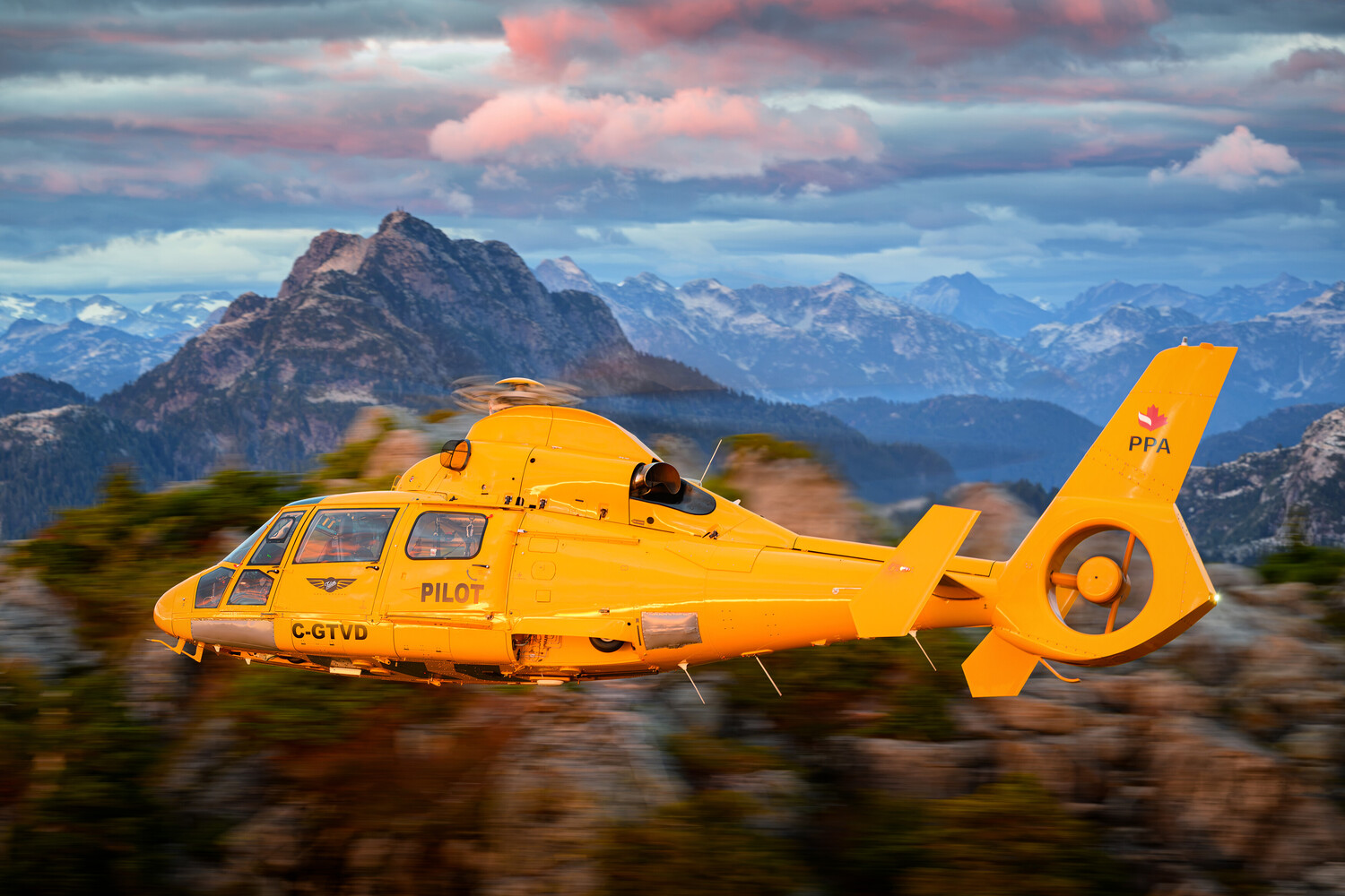 Yellow rescue helicopter in flight with snow-capped Alpine mountains and dramatic sky in background