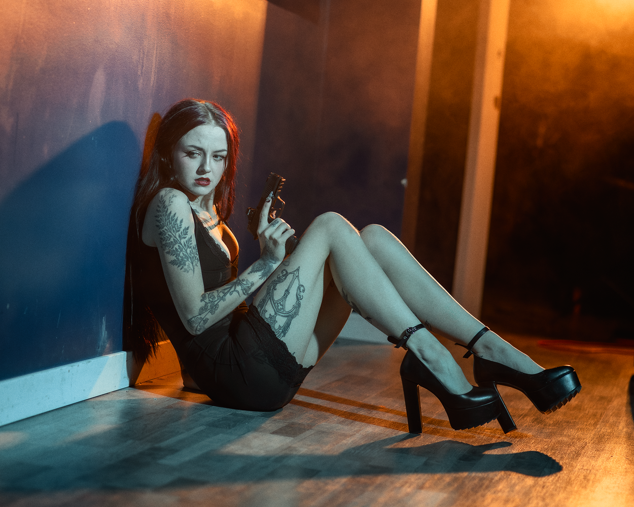 Woman with tattoos sitting against warm-lit wall, holding cigarette in dramatic studio lighting