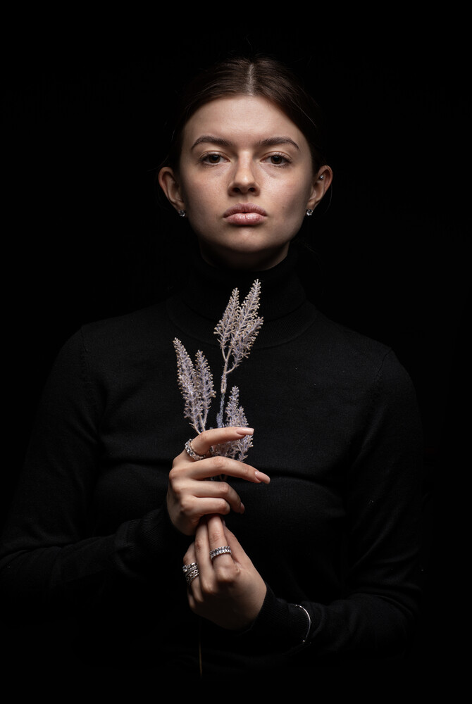 Young person in black shirt holding dried wheat stalks against dark background