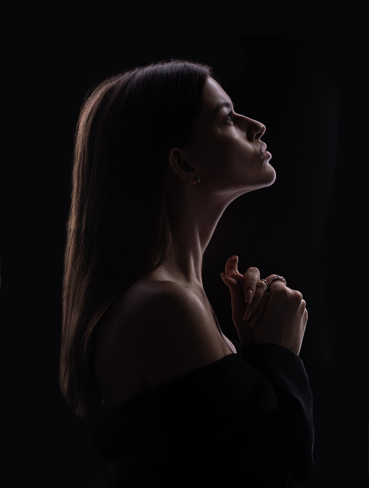 Woman in profile with hands clasped, backlit against dark background with rim lighting