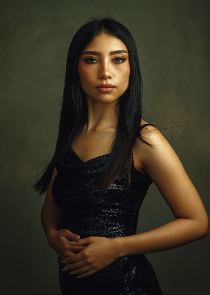 Woman with long dark hair wearing black sleeveless top against muted green background