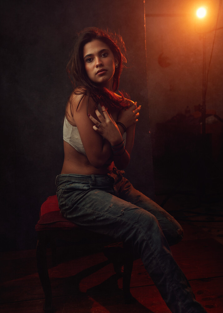 Woman seated on red chair in dramatic warm studio lighting