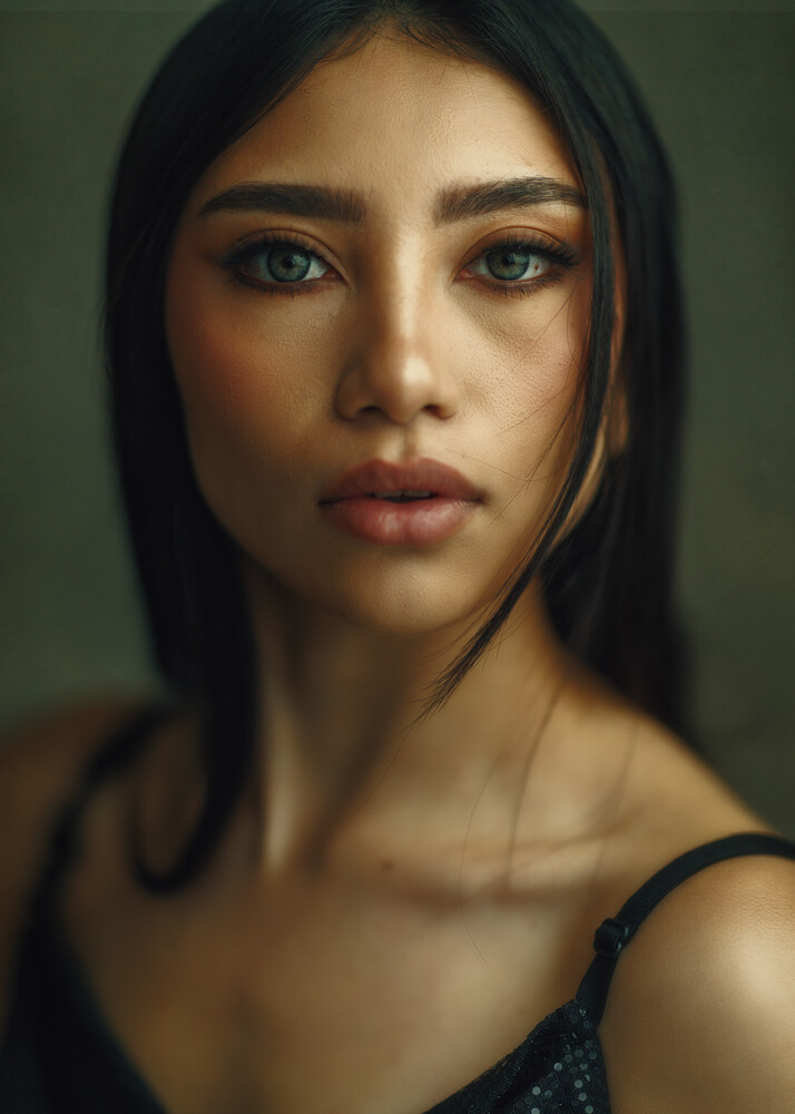 Portrait of a woman with long dark hair against a muted green background, wearing a dark sleeveless top