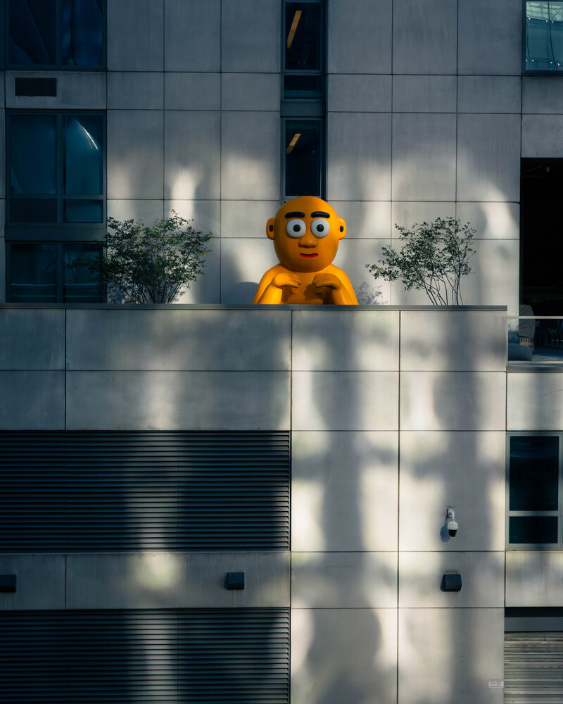 Large yellow cartoon character figure mounted on modern glass building facade