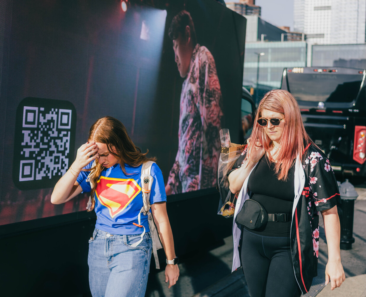 Two people standing outdoors in front of a large projection screen displaying a QR code and portrait imagery