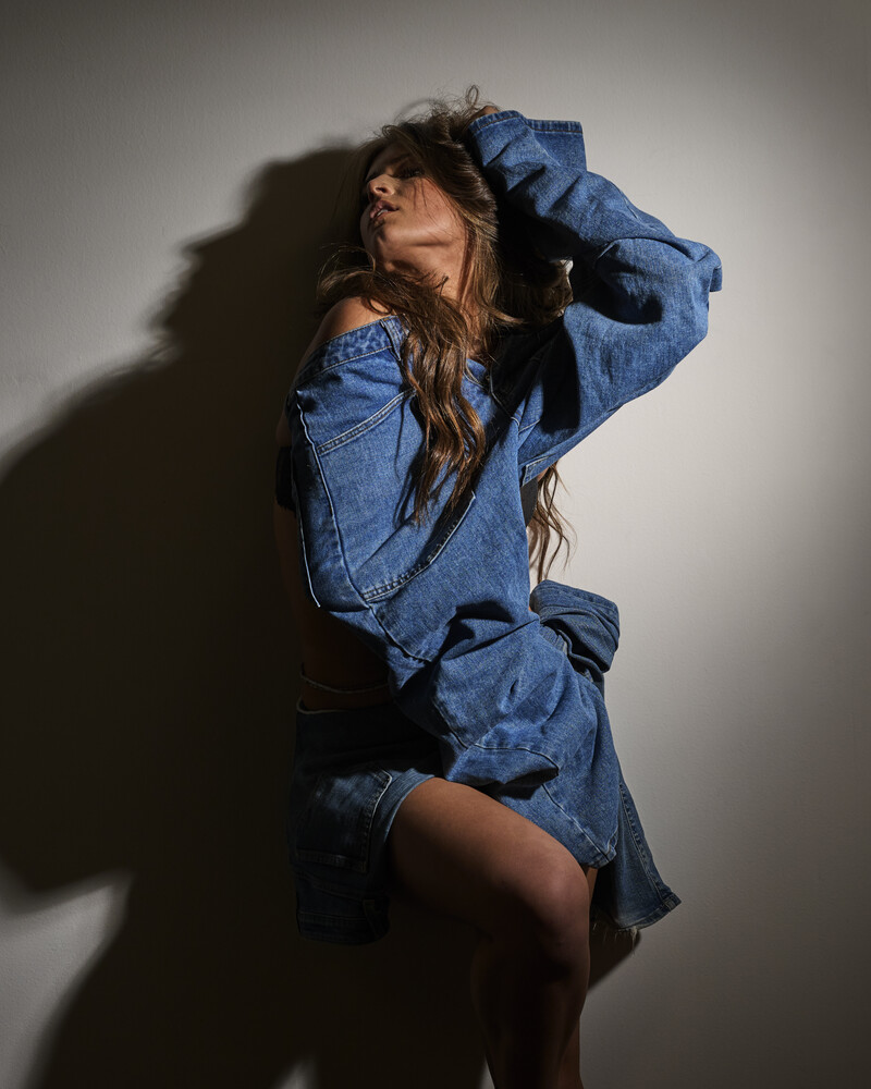 Woman in denim shirt posing against neutral background with dramatic side lighting