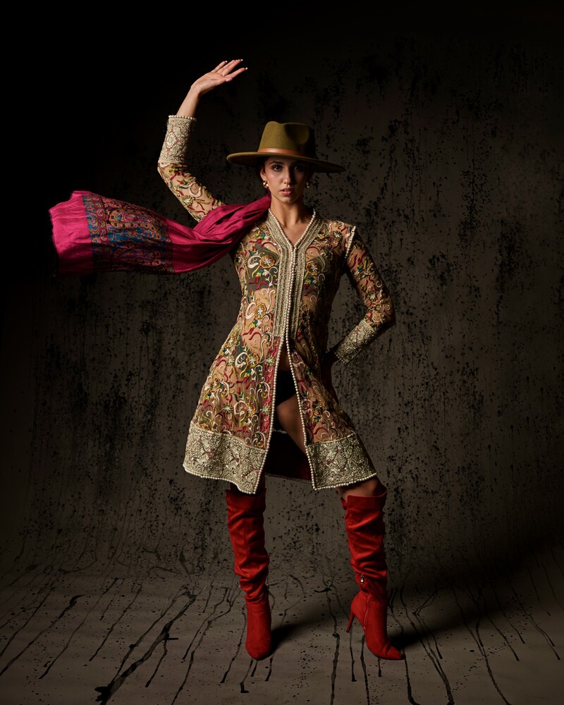 Person in ornate embroidered coat and red boots striking a theatrical pose with pink fabric flowing