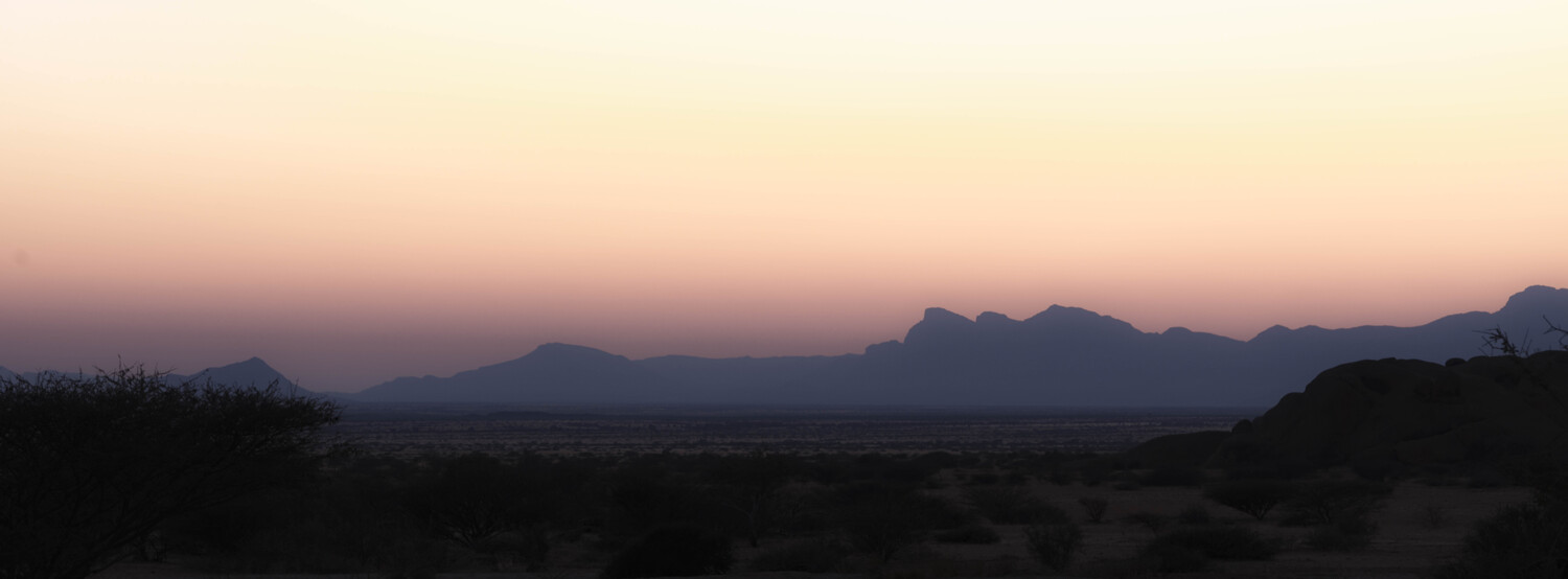 Desert landscape at dusk with distant mountain silhouettes against pink sky