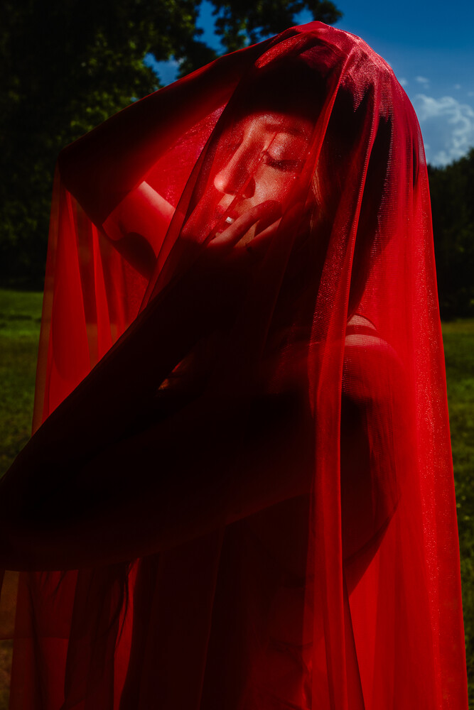 Person draped in flowing red fabric with dramatic side lighting against outdoor setting