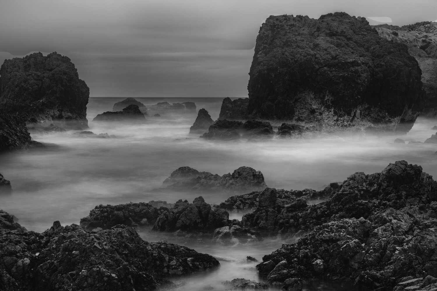 Misty seascape with dark rocky outcroppings and smooth water from long exposure