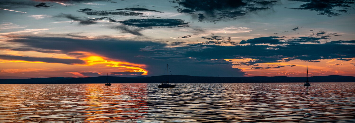 Sailboats anchored in calm water at sunset with dramatic golden and orange sky