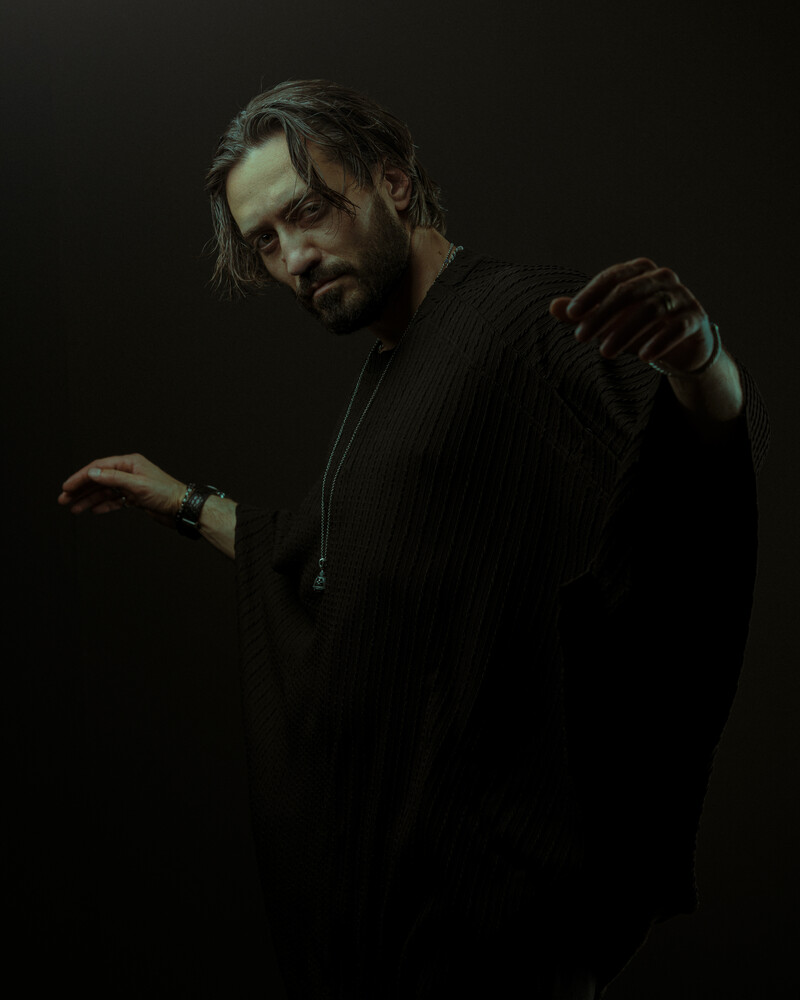 Man in dark clothing with dramatic side lighting against black background