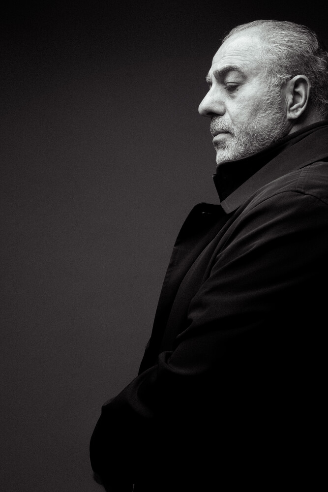 Profile portrait of a man in dark clothing against a black background