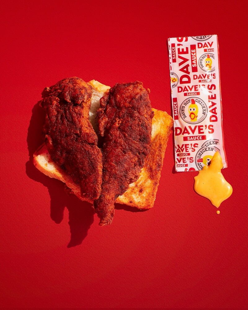 Fried chicken sandwich with hot sauce packet on bright red background