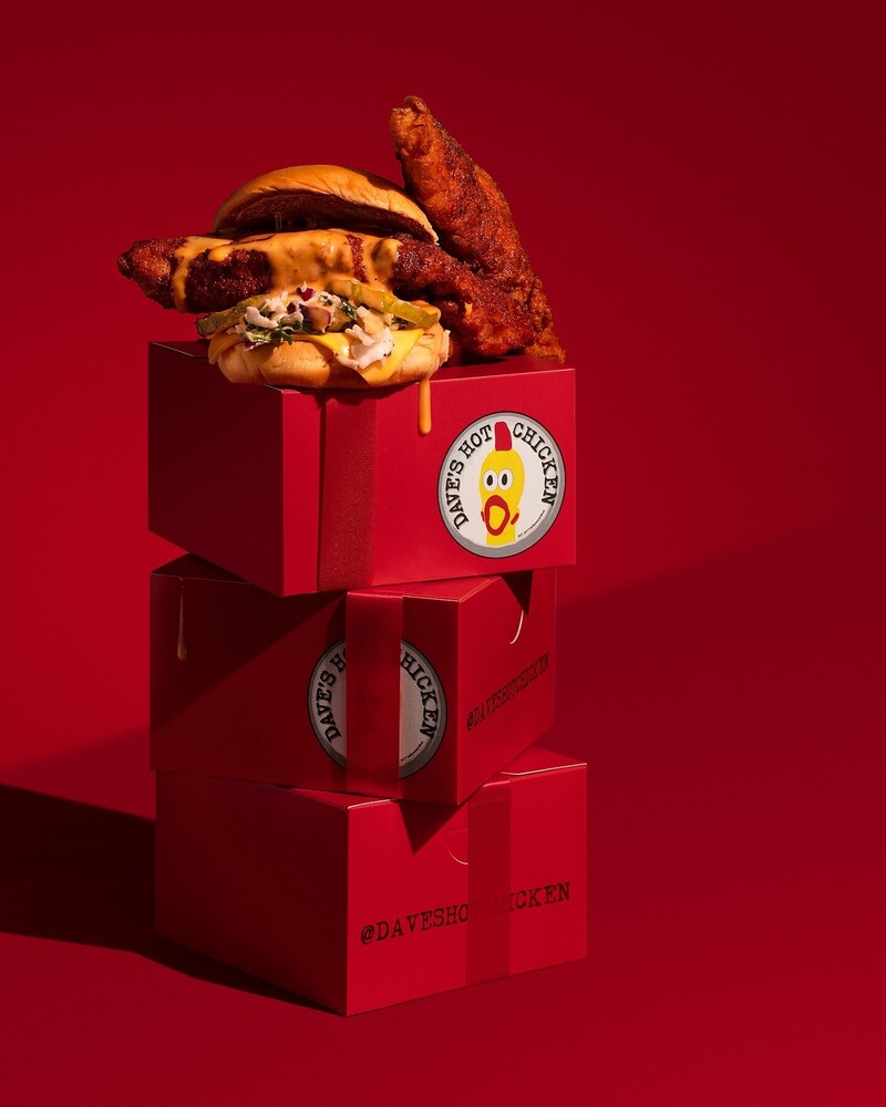 Stacked red boxes with a roasted chicken and herbs on top against a red background