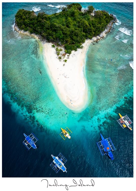 Aerial view of a heart-shaped island with white sand beach surrounded by turquoise water and traditional boats