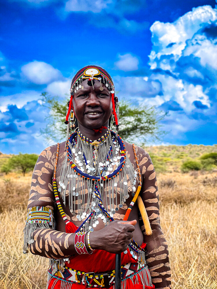 Maasai woman in traditional beaded regalia standing in savanna landscape