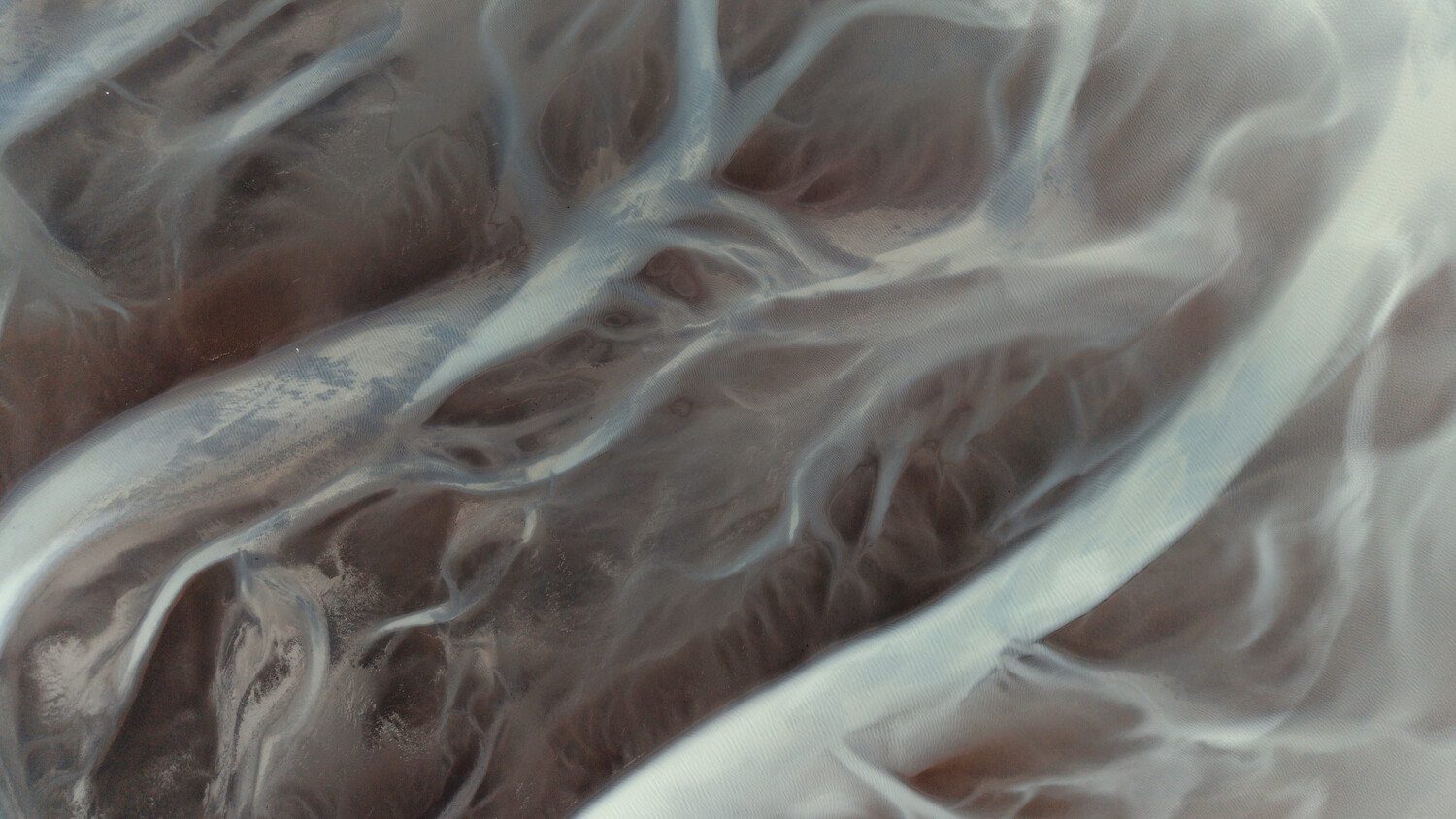 Aerial view of meandering river channels and ridges creating abstract patterns across desert landscape