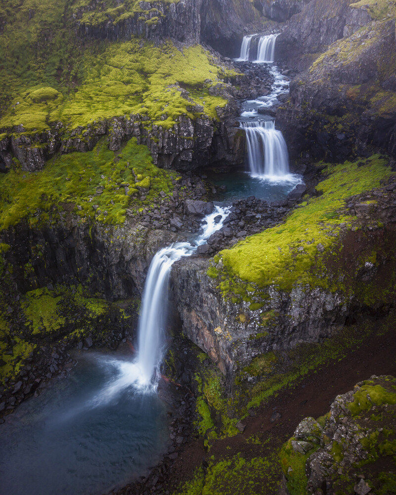 Cascading waterfalls flowing through moss-covered rocky terrain with lush green vegetation