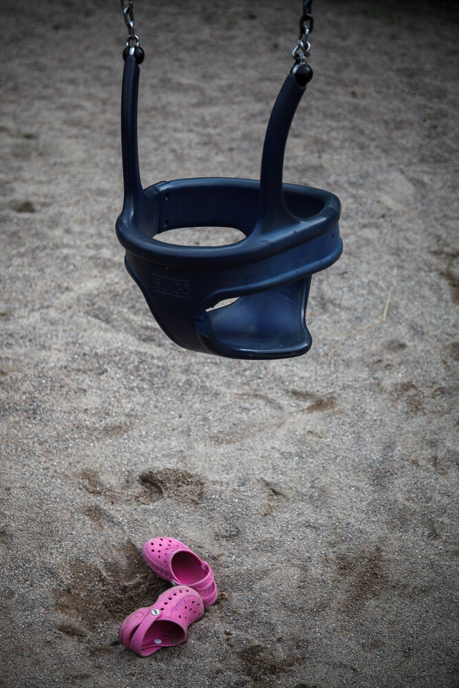 Empty blue swing seat on sand with pink shoes below
