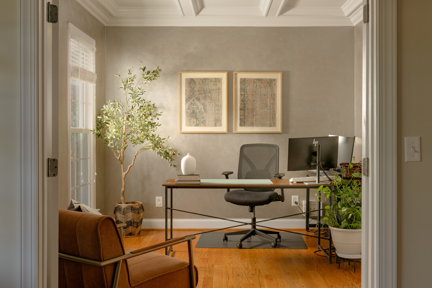 Modern home office with desk, monitor, black chair, and potted plants near windows