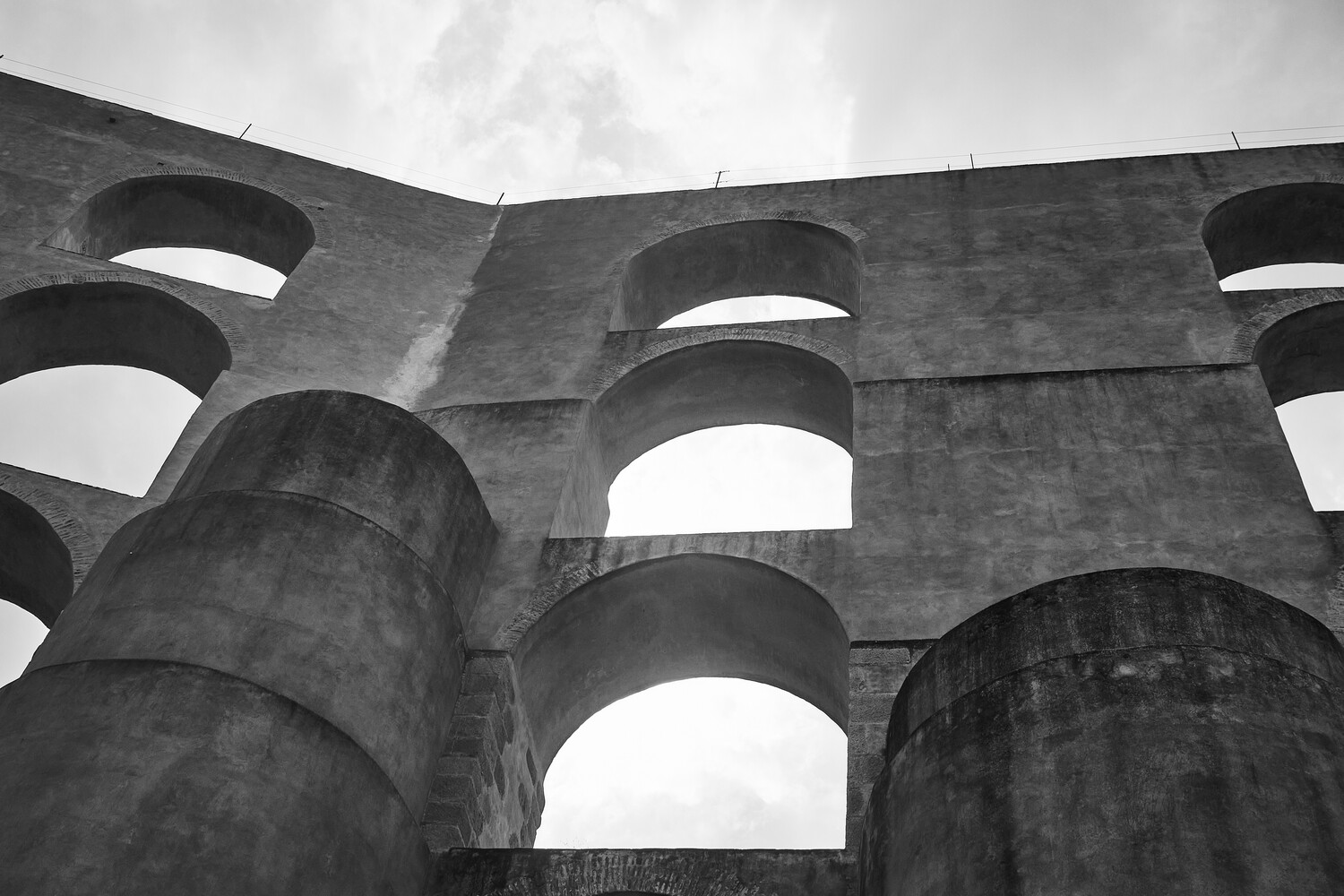 Brutalist concrete structure with large cylindrical columns and arched cutouts against cloudy sky