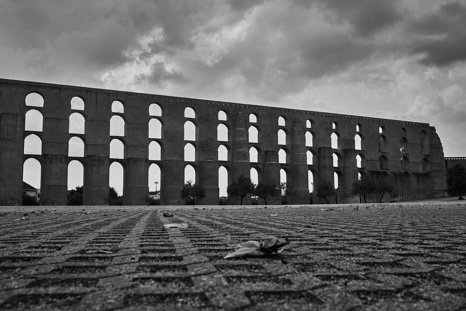 Massive Roman aqueduct with repeating arched openings under dramatic cloudy sky